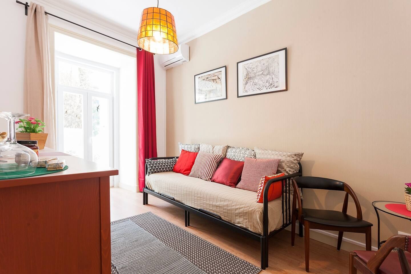 Une pièce chaleureuse avec un canapé, une table à manger et une chaise. Il y a une fenêtre avec des rideaux, une lampe suspendue et deux tableaux encadrés au mur.