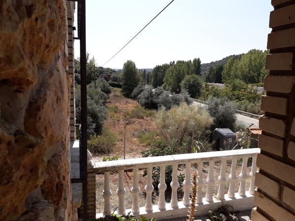 A balcony with a white balustrade overlooking a hilly landscape with trees and a road.