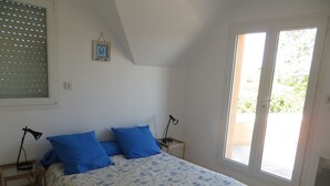 Un dormitorio con cama, dos lámparas de noche, una ventana con persianas y una puerta que da al exterior.