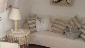 A cozy room with a white sofa, striped cushions, a small round table with a lamp, and a painting on the wall.
