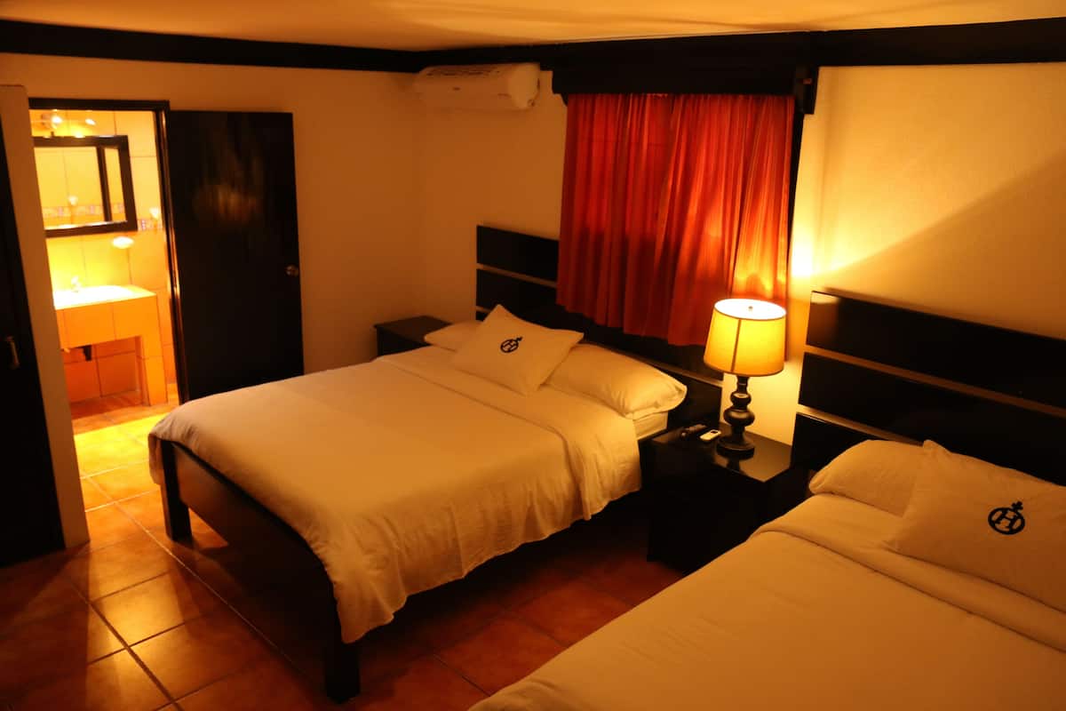 Een hotelkamer met twee bedden, een nachtkastje met een lamp, en een badkamer zichtbaar door een open deur, met een rood gordijn.