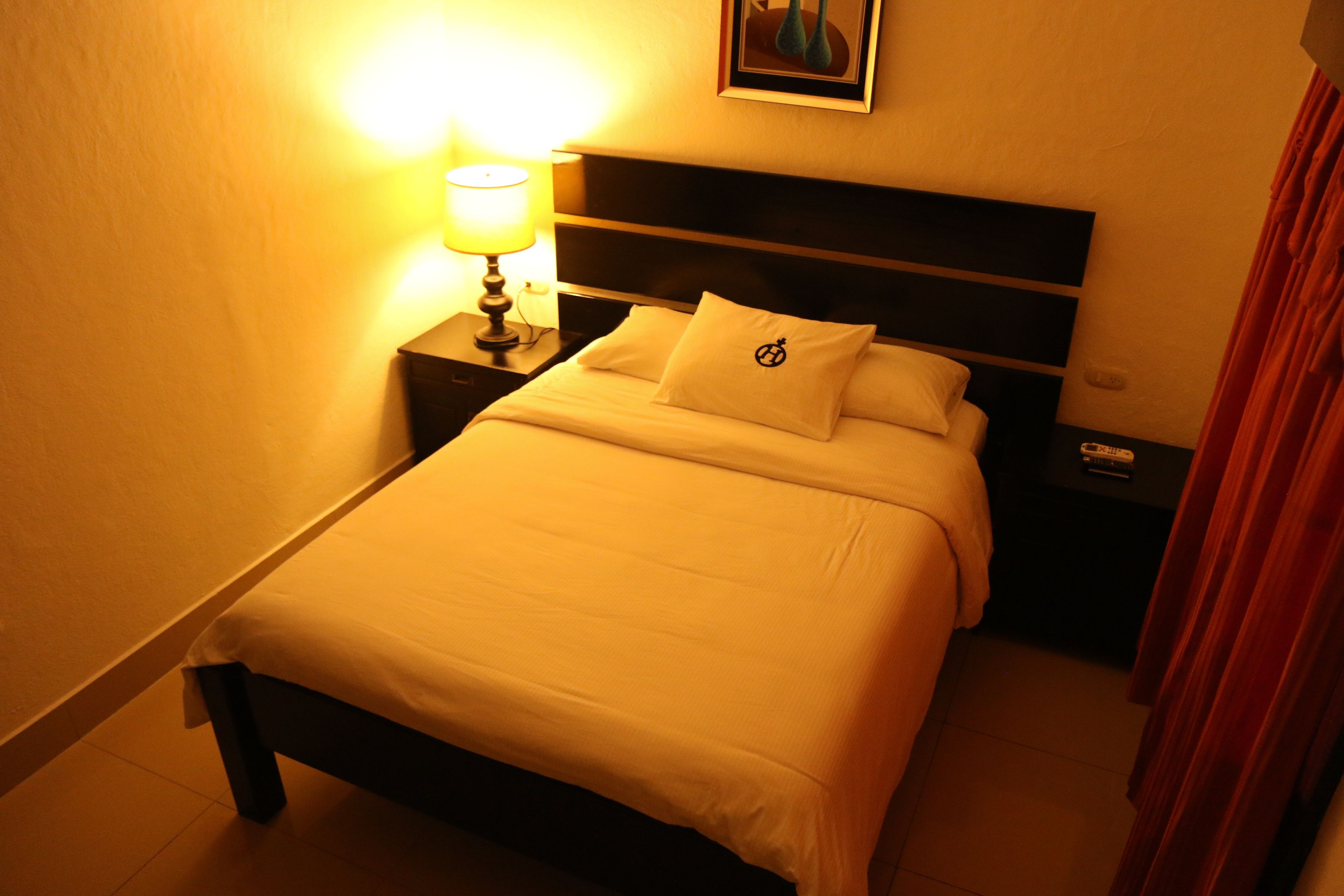 A neatly made bed with a headboard, a bedside lamp, and a nightstand with a remote control.