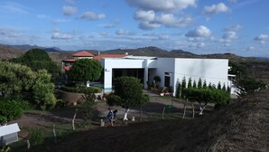 Un edificio moderno con techo plano, rodeado de exuberante vegetación y montañas al fondo.