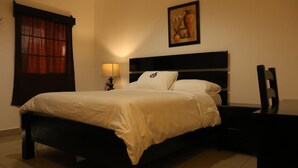 Una cama bien hecha con cabecera, una mesita de noche con lámpara y un cuadro en la pared.