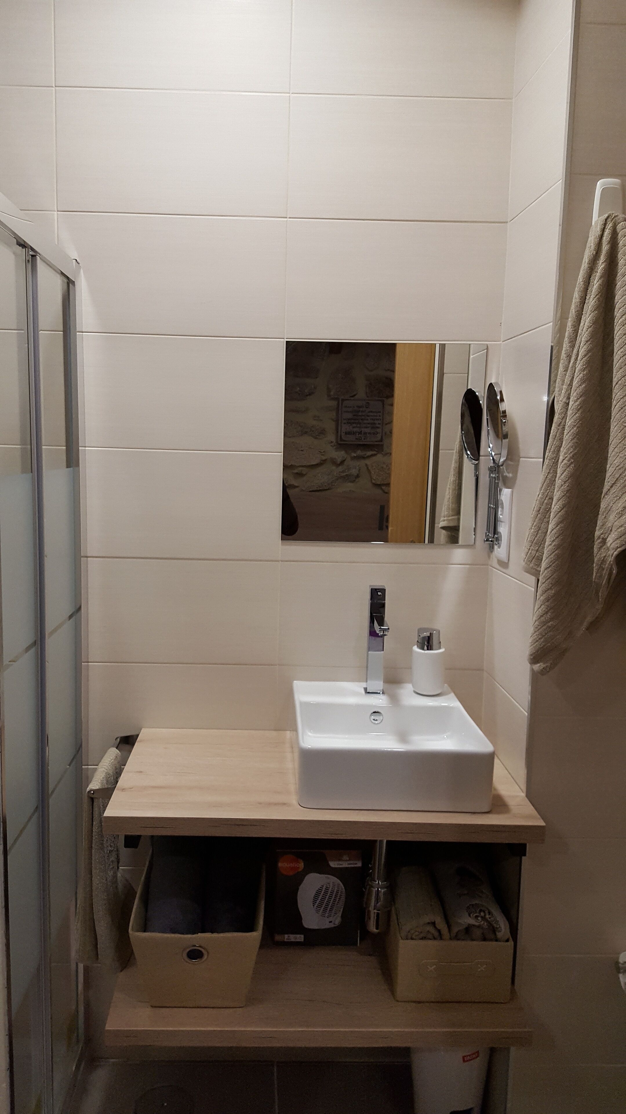Ein Badezimmer mit einem weißen Waschbecken, einem Spiegel und einem Handtuch, das an der Wand hängt. Unter dem Waschbecken befinden sich Aufbewahrungsboxen.