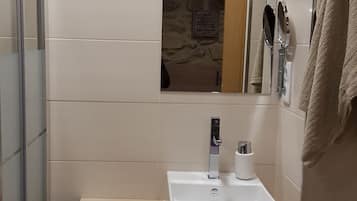 Ein Badezimmer mit einem weißen Waschbecken, einem Spiegel und einem Handtuch, das an der Wand hängt. Unter dem Waschbecken befinden sich Aufbewahrungsboxen.