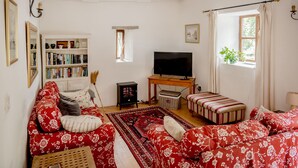En stue med sofa, fjernsyn, bogreol og et vindue med gardiner.