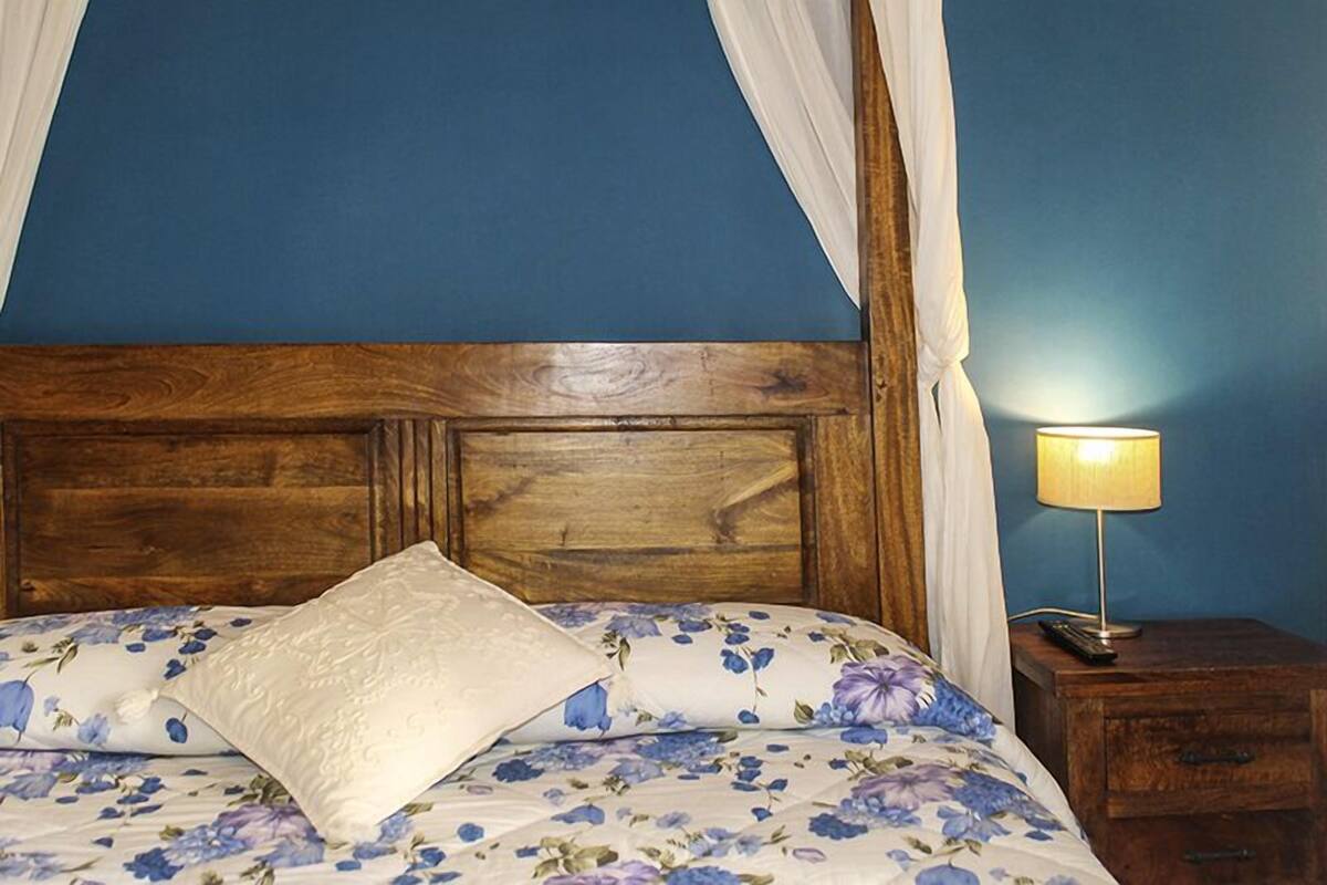 A bed with a floral bedspread, a wooden headboard, and a bedside table with a lamp.