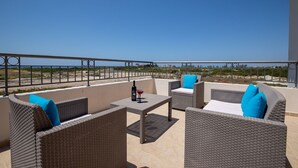 Ein Balkon mit Korbmöbeln, einem Tisch und einer Weinflasche.