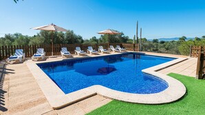 Une piscine rectangulaire bordée de carreaux, entourée d’une clôture en bois et dotée d’une terrasse en bois avec des chaises longues.