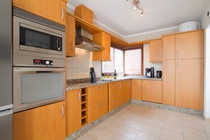 Cozinha moderna com armários de madeira, eletrodomésticos de aço inoxidável e bancada de granito.