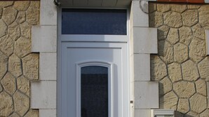 A white door with a small window above it, set in a stone wall with a brick section above.