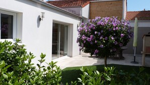 A modern house with a white exterior, a tiled roof, and a small garden with green grass and purple flowers.