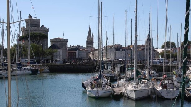 A marina with multiple sailboats docked, a historic building with a tower, and a clear sky.