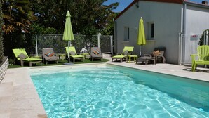 A swimming pool with clear blue water, surrounded by lounge chairs and umbrellas.