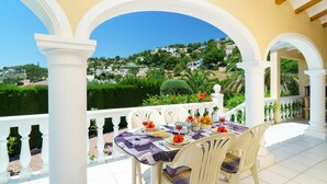 Une terrasse avec une table dressée pour le dîner, des colonnes blanches et une vue sur une ville perchée sur une colline.
