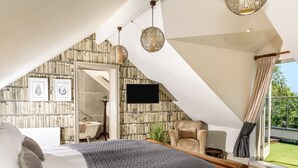 Une chambre avec un plafond en pente, un lit, une chaise, un téléviseur et une vue sur l’extérieur.