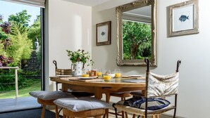Un coin repas avec une table ronde en bois, quatre chaises en bois avec des coussins, un vase de fleurs et un tableau encadré au mur.