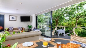 Un salon moderne avec un canapé, une table à manger où sont disposés des aliments pour le petit-déjeuner, et un balcon agrémenté de mobilier d’extérieur.