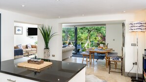 Une cuisine moderne dotée d’un îlot central, un coin repas avec une table et des chaises, et un espace de vie avec un canapé et un téléviseur.