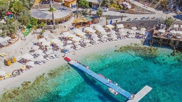 Luchtbeeld van een strand met een pier die zich uitstrekt over helder turquoise water.