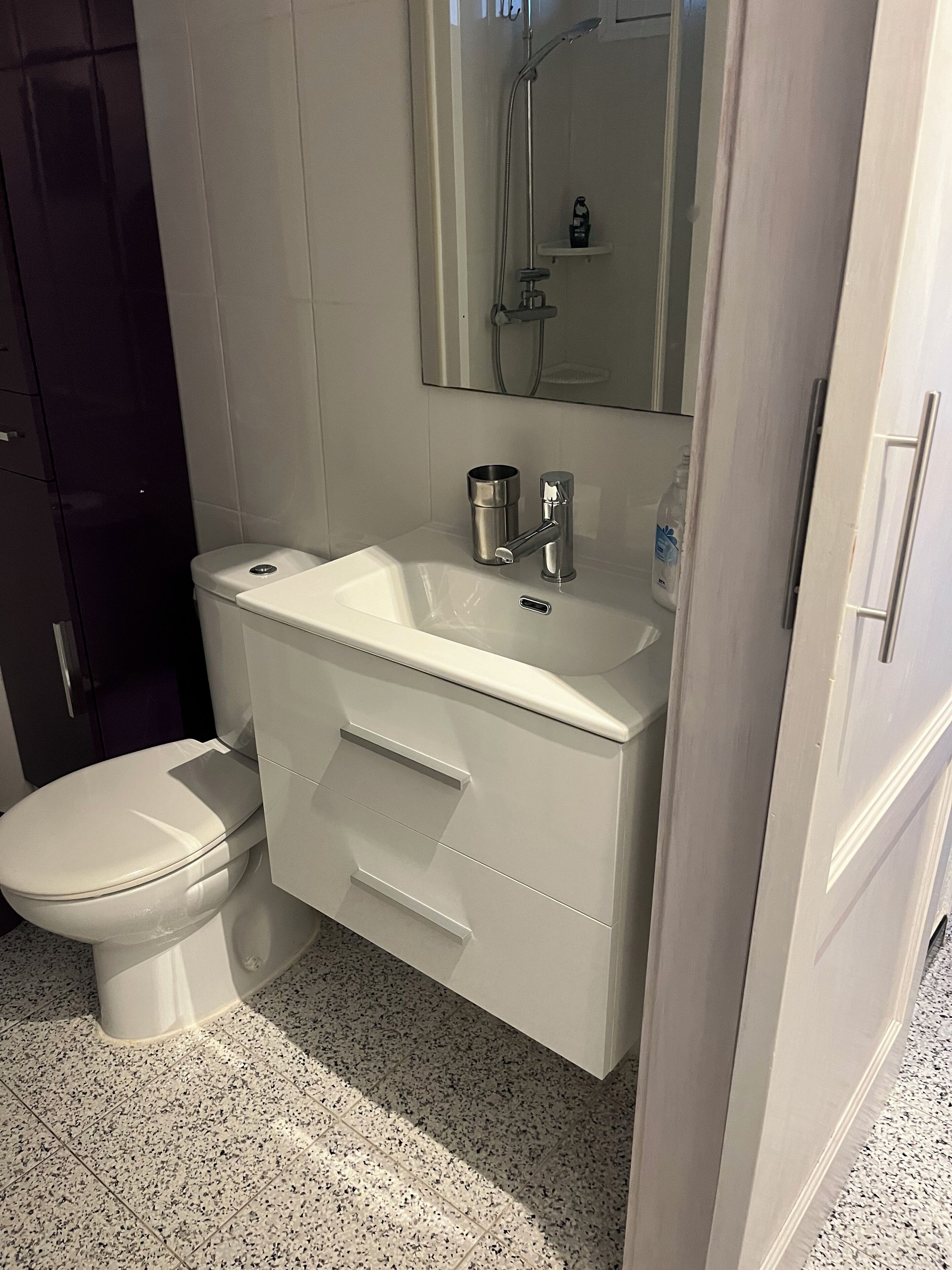 Een badkamer met een wit toilet, een wastafel met een spiegel erboven en een zichtbare douchecel in de spiegeling.