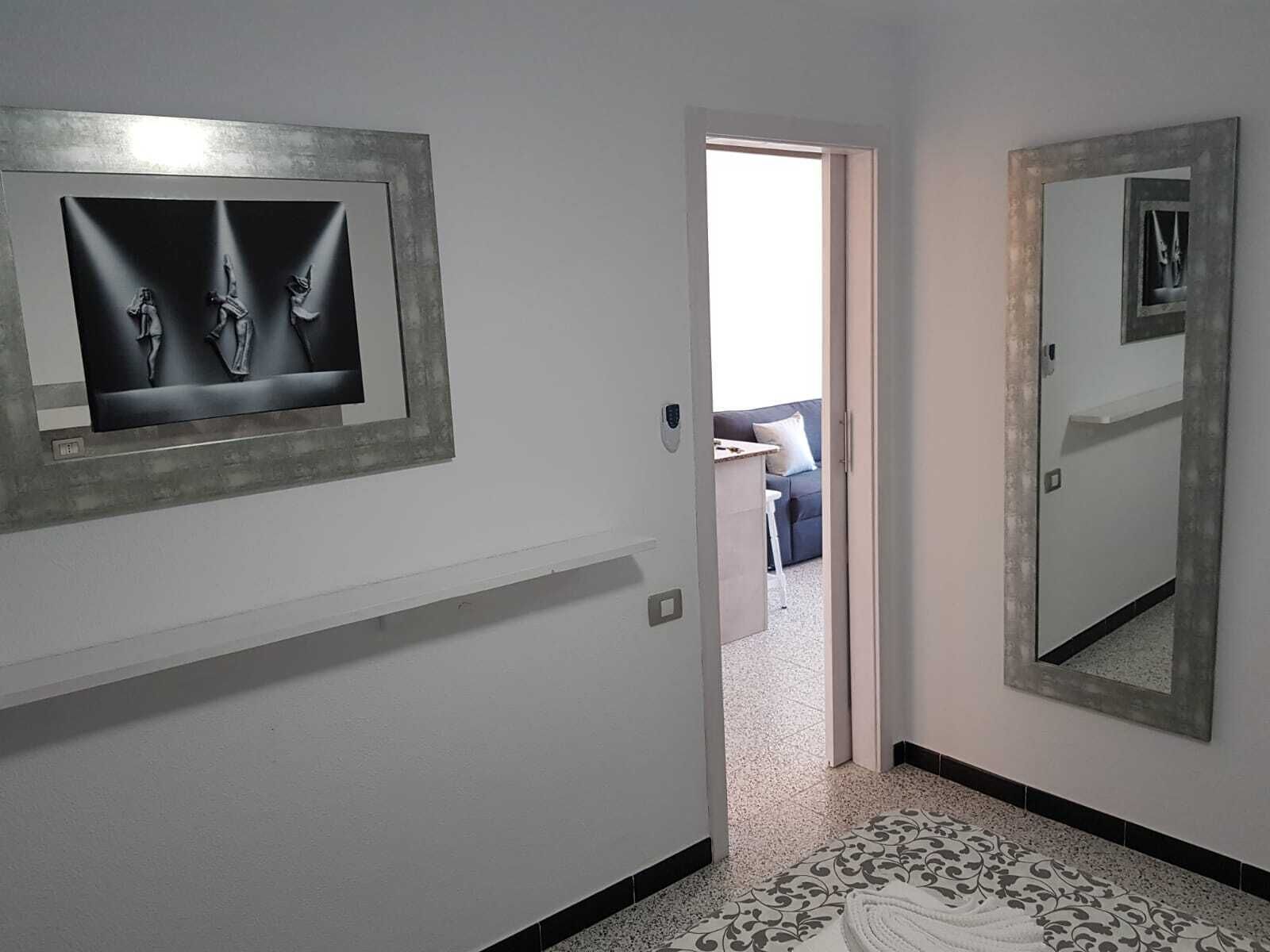 Un pasillo con una puerta que da a una sala de estar, un espejo grande y una obra de arte enmarcada en la pared.