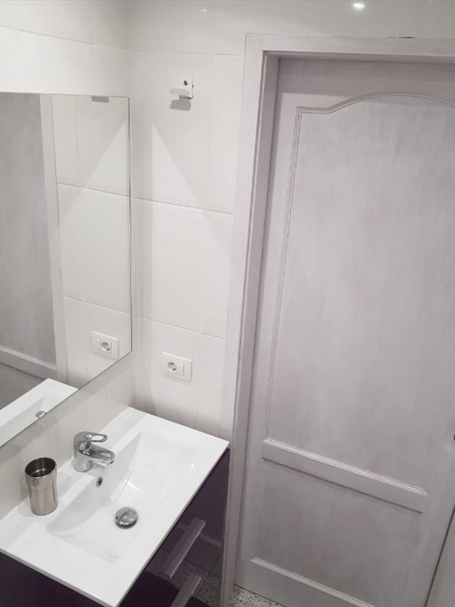 A bathroom with a white sink, mirror, and door.