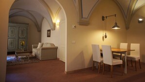 A dining area with a wooden table and white chairs, a sofa, and a decorative wall lamp.