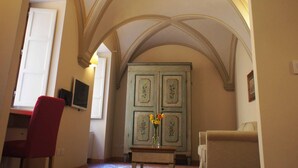 A room with a high arched ceiling, a desk with a red chair, a cabinet with floral patterns, and a sofa.