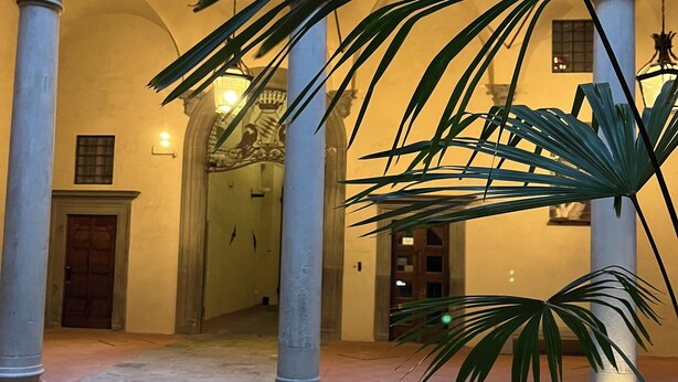 A courtyard with arches, columns, and potted plants.