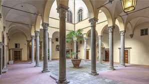 A spacious courtyard with columns, a central plant, and a tiled floor.