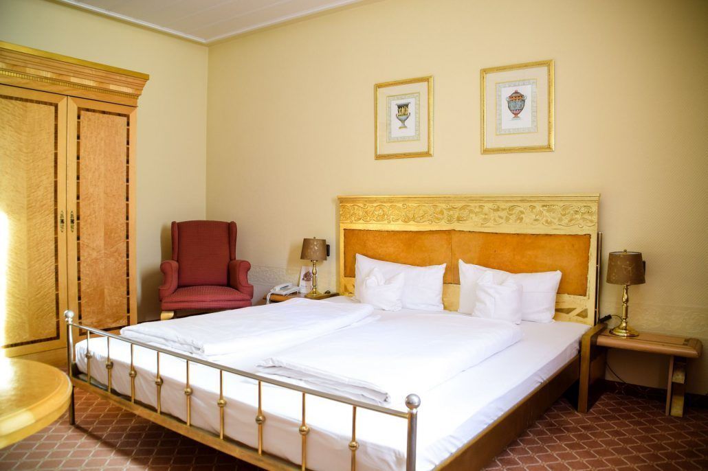Habitación de hotel con una cama grande, un sillón rojo, dos mesitas de noche con lámparas y un armario de madera.