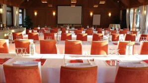 Un salón de conferencias con filas de mesas y sillas, una pantalla de proyector e iluminación ambiental.
