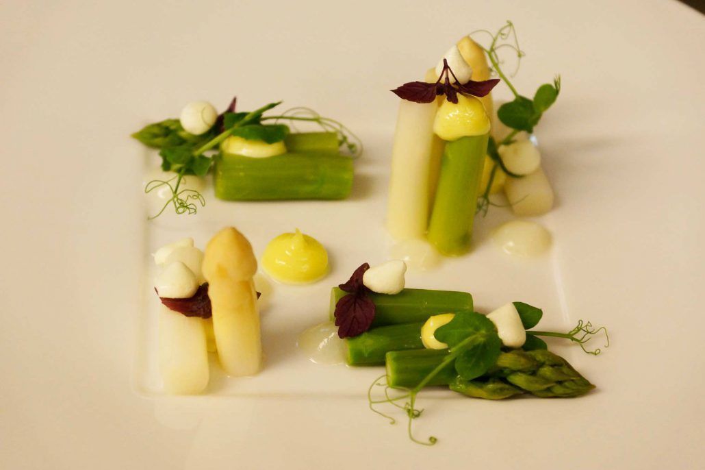 A white plate with various food items including asparagus, cream, and small dollops of sauce.