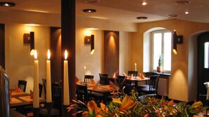 Un interior de restaurante con mesas iluminadas por velas, una columna central y un arreglo floral.