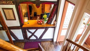 Una escalera de madera con una alfombra roja que lleva a un cuarto con una mesa de madera, un certificado enmarcado y una planta.