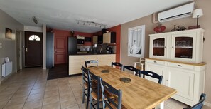 Una cocina con comedor, que incluye una mesa y sillas de madera, un refrigerador, armarios y un mueble blanco con puertas de vidrio.