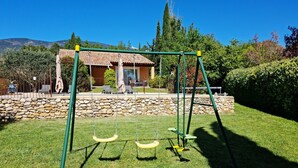 A grassy area with a swing set and a stone wall. - Air-conditioned house 1 km Bédoin/Ventoux - Private/heated swimming pool - Wifi (Bédoin)