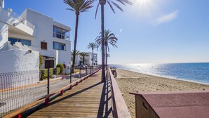 Une promenade en bois menant à une plage bordée de palmiers et surmontée d’un bâtiment blanc doté de balcons.