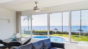 Un salon moderne doté d’une grande fenêtre, d’un canapé en cuir noir, d’une table basse en verre et offrant une vue sur une piscine et l’océan.