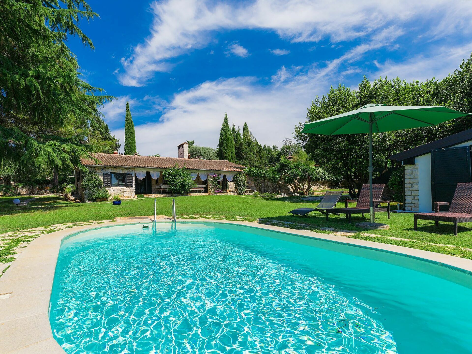 A swimming pool with clear blue water, surrounded by a well-maintained lawn and trees. There are lounge chairs and a covered seating area.