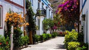 Une rue étroite bordée de bâtiments blancs, dont certains sont dotés de balcons et de jardinières fleuries.