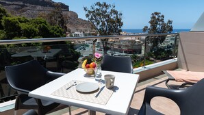 Un balcon avec une table dressée pour deux personnes, offrant une vue sur une ville côtière et une montagne.