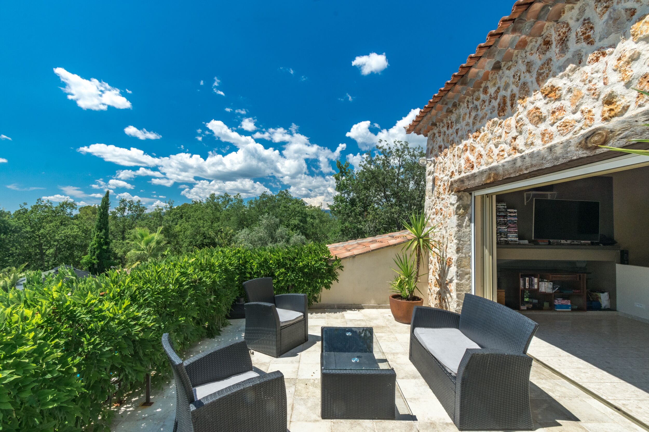 An outdoor patio with wicker furniture, a TV, and a stone wall.
