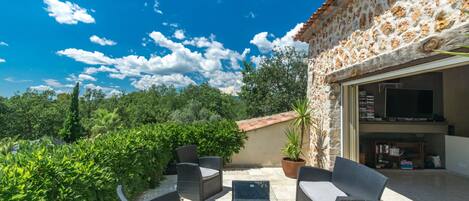 An outdoor patio with wicker furniture, a TV, and a stone wall.