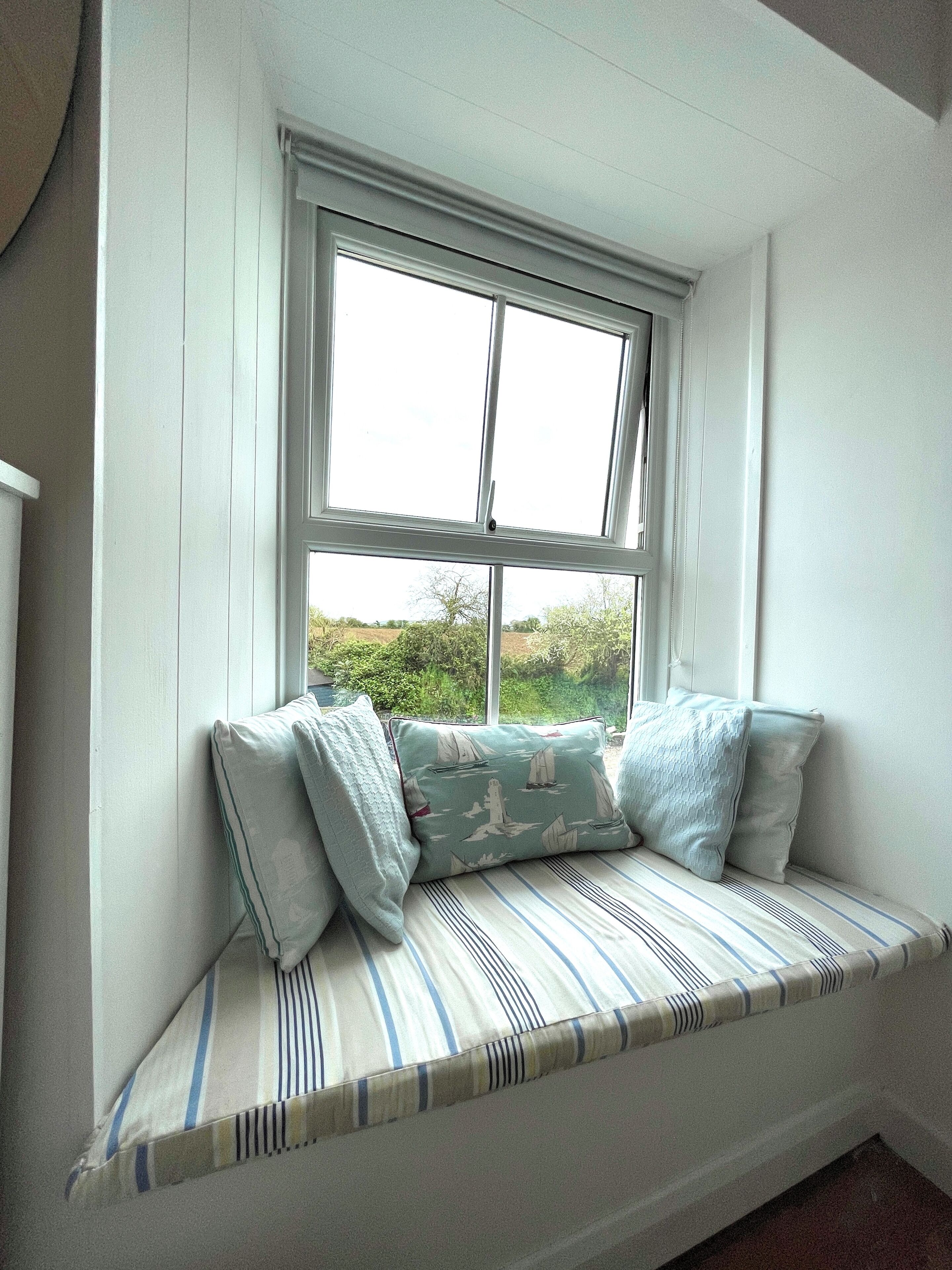 A room with a window seat featuring striped cushions and a cushion with a sailboat pattern.