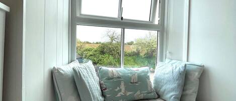 A room with a window seat featuring striped cushions and a cushion with a sailboat pattern.