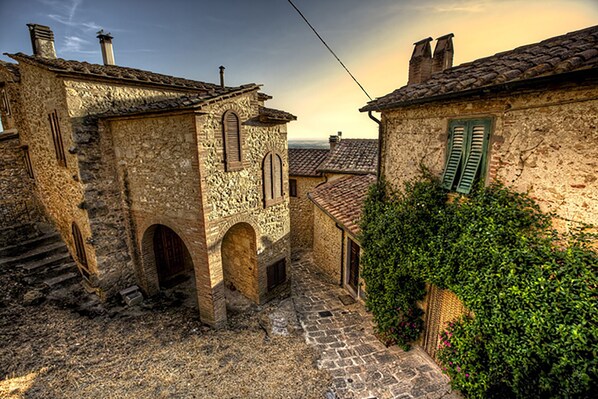 A narrow cobblestone street with stone buildings, arched doorways, and green shutters.