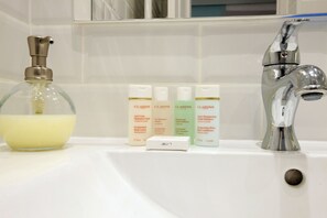 Ein Waschbecken mit einer Glas-Seifenspender, einem Chrom-Wasserhahn und drei Flaschen Clarins Körperpflegeprodukte.